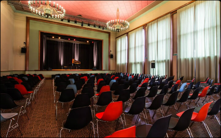 Salle de spectacle de Renens vue de côté, fauteuils rouges et noirs et hautes fenêtres à rideaux