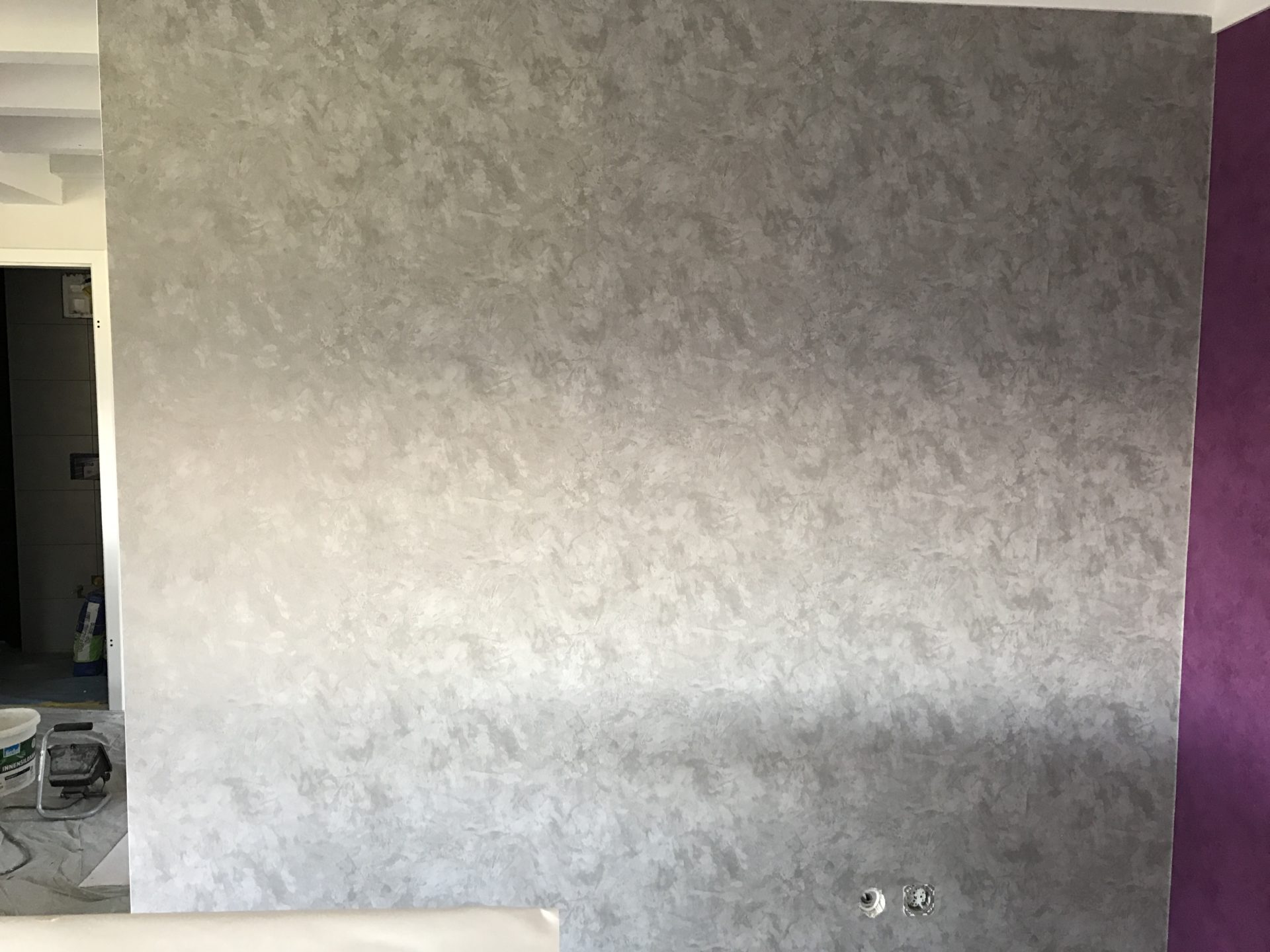 Mur fini en enduit décoratif effet nuagé gris argenté, bordé d'un pan de mur prune