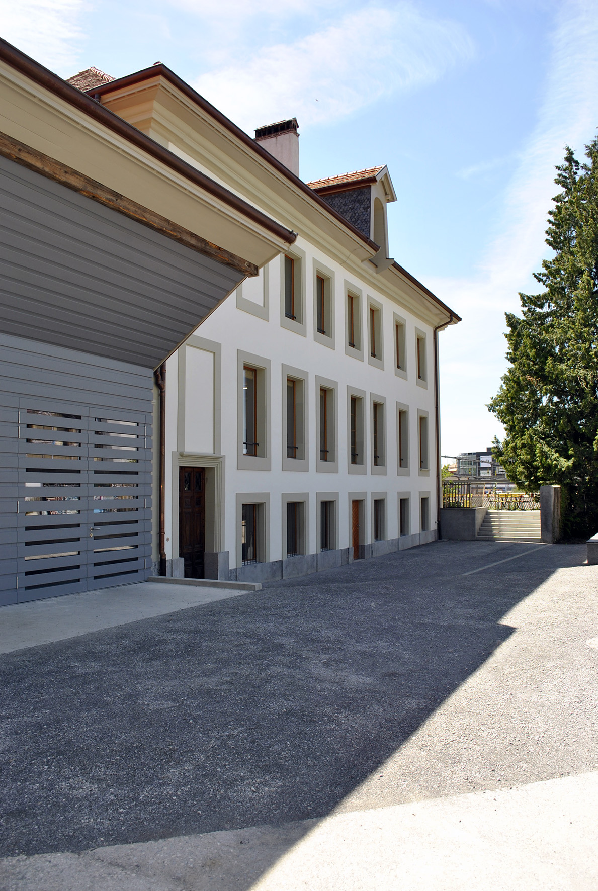 Bâtiment annexe de la Ferme des Tilleuls, crépi blanc et bardage gris le long de la cour