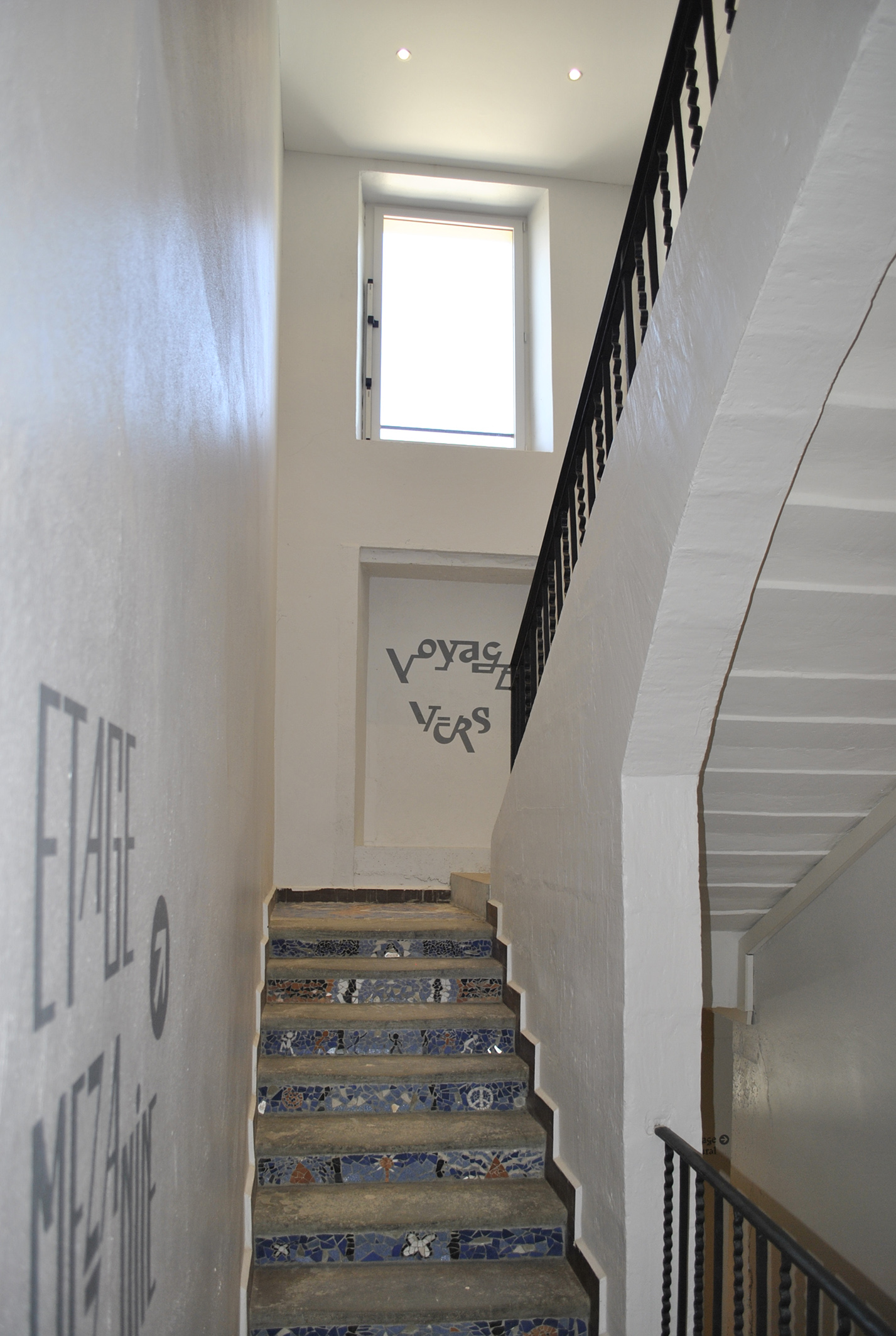 Cage d'escalier blanche de la Ferme des Tilleuls, marches en pierre et inscriptions murales