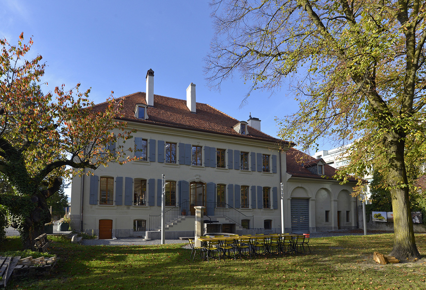 Ferme des Tilleuls en automne, façade à volets bleus derrière les arbres