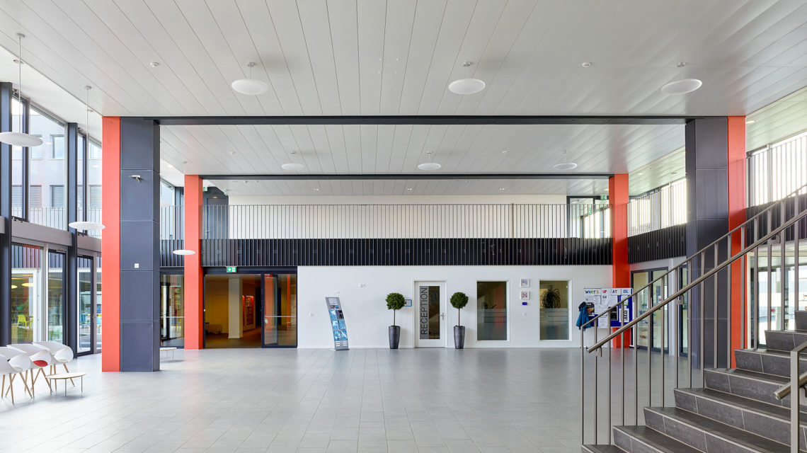 Hall d'entrée vitré de l'International School of Lausanne, piliers rouges et bleus et escalier