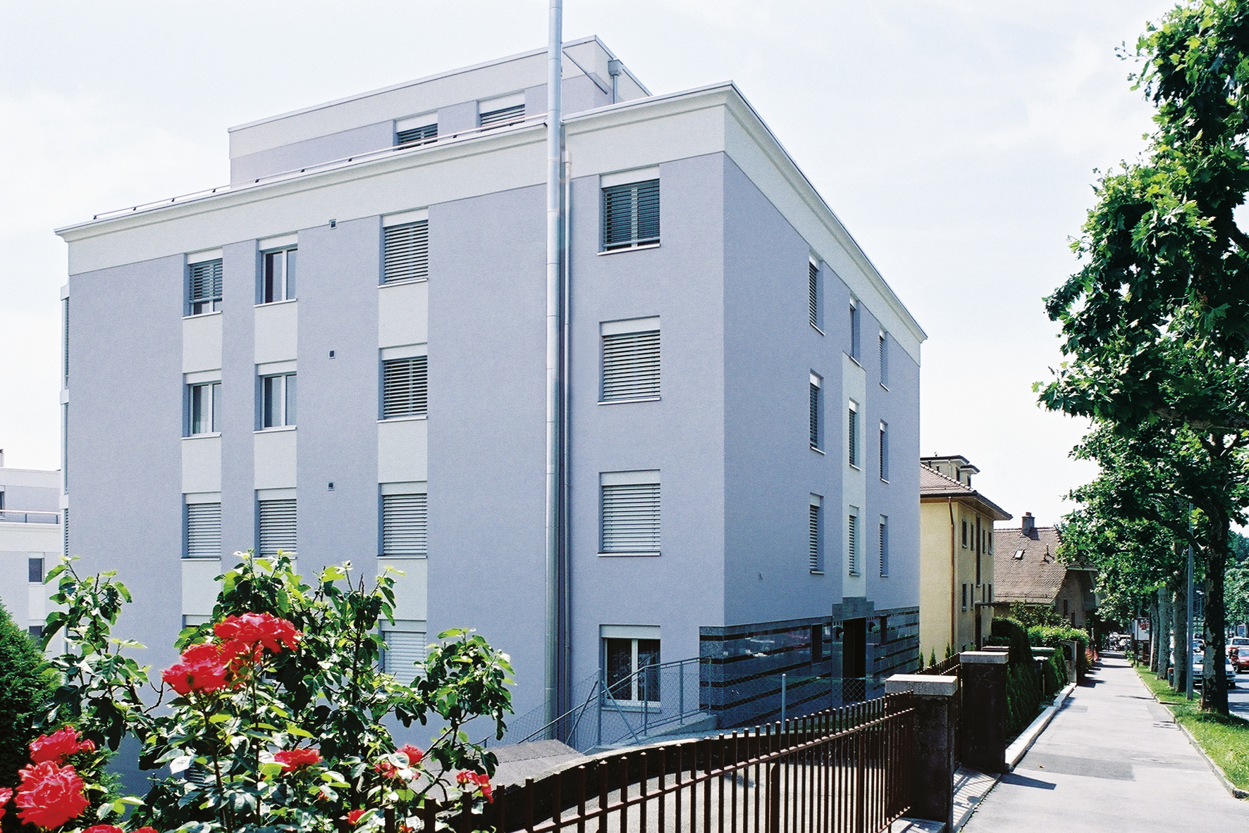 Immeuble des Résidences des Figuiers vu depuis la rue, façade claire et rosiers en fleurs