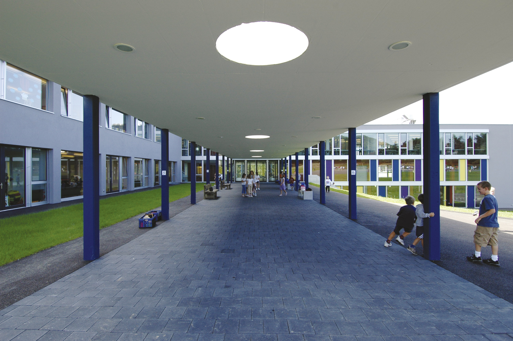 Préau couvert de l'International School of Lausanne aux piliers bleus, avec des élèves qui jouent