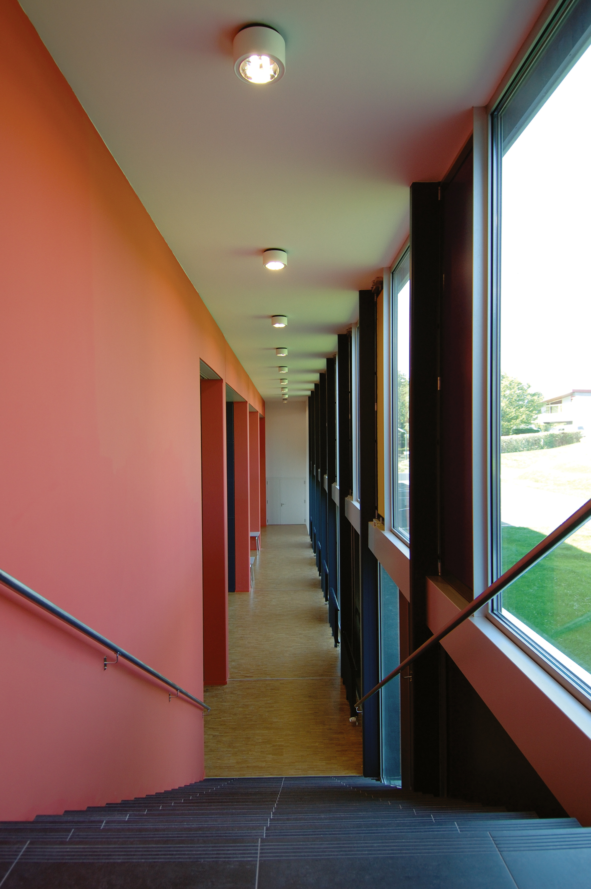 Couloir en gradins de l'International School of Lausanne, mur orange et baies vitrées sur le parc