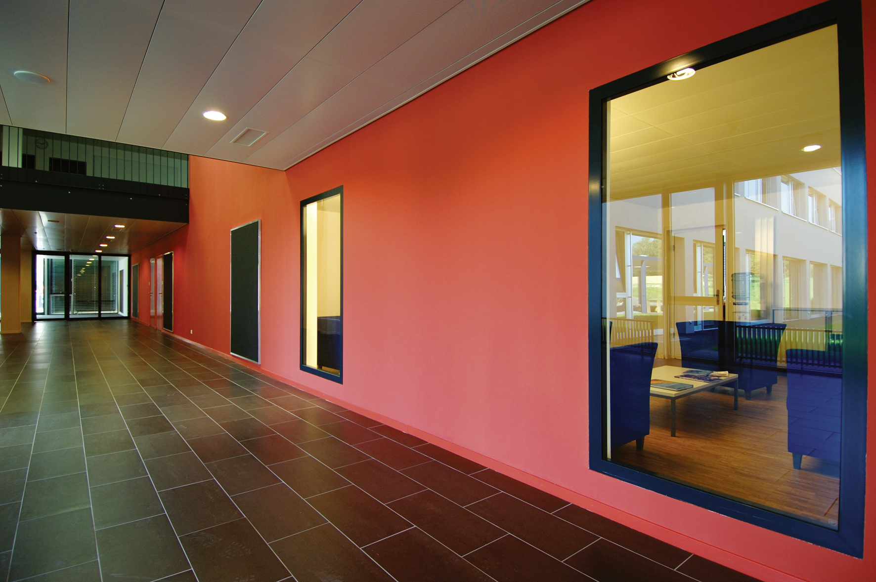 Couloir de l'International School of Lausanne, mur rouge et grande baie vitrée sur une salle de travail