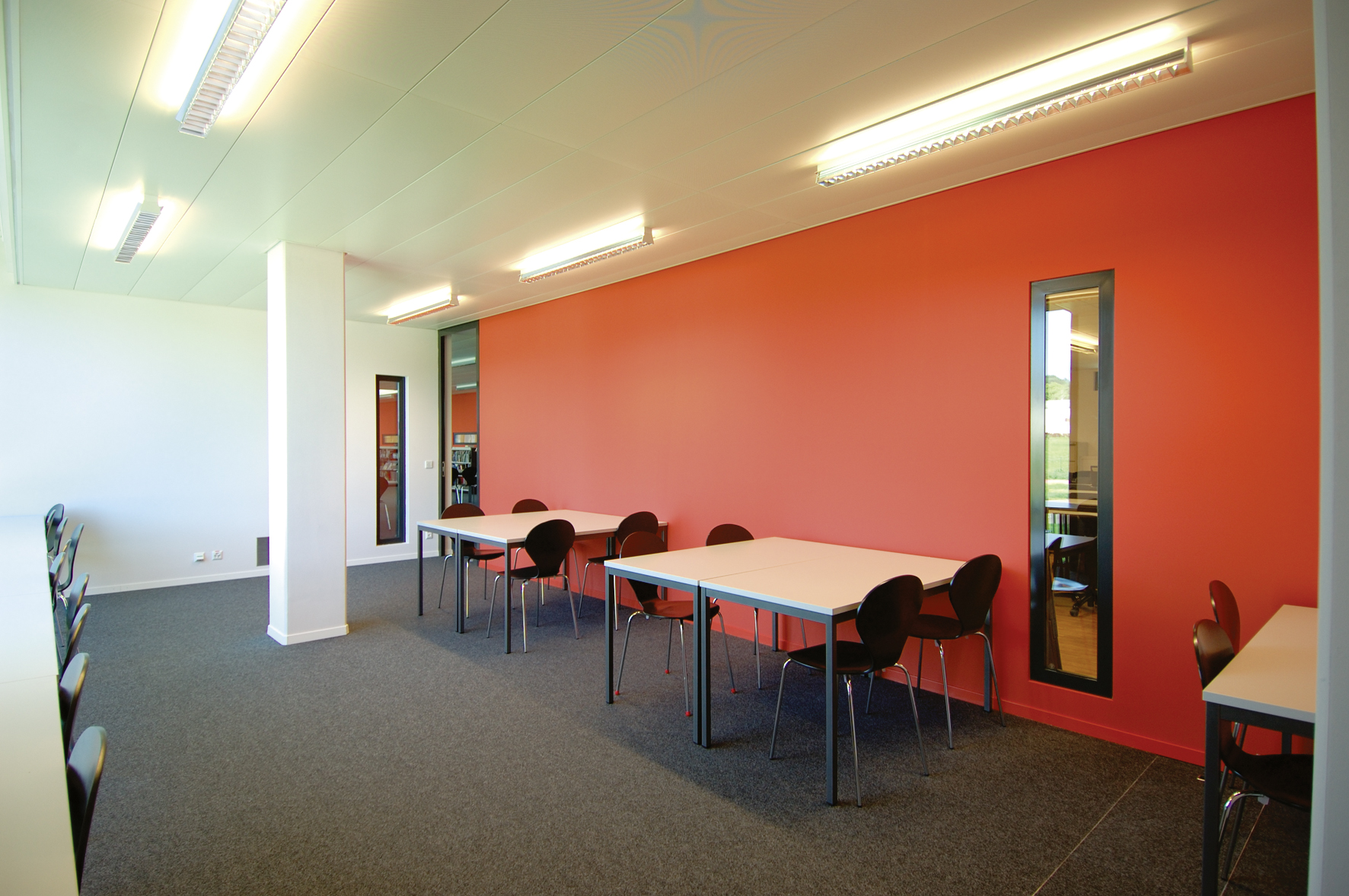 Salle de réunion de l'International School of Lausanne, mur orange, tables blanches et chaises noires