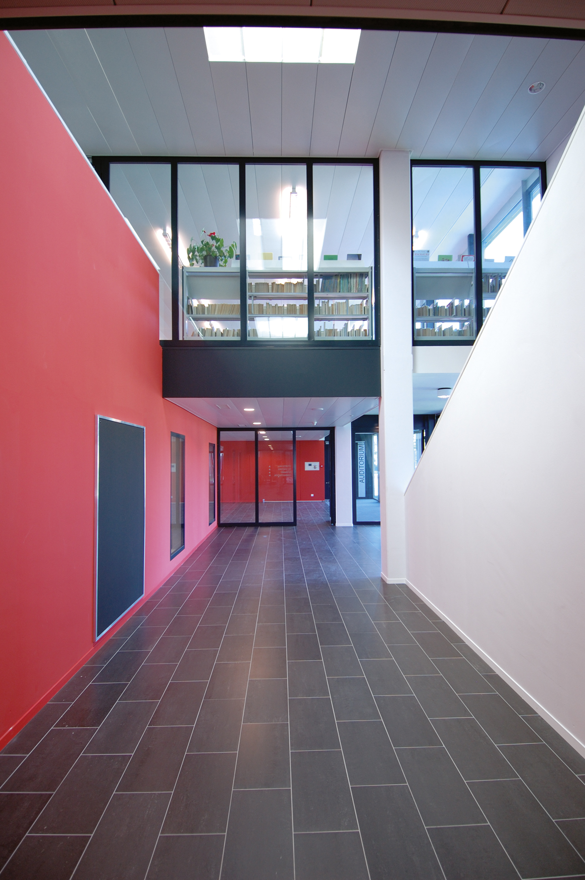 Hall à double hauteur de l'International School of Lausanne, mur rouge et bibliothèque vitrée en mezzanine