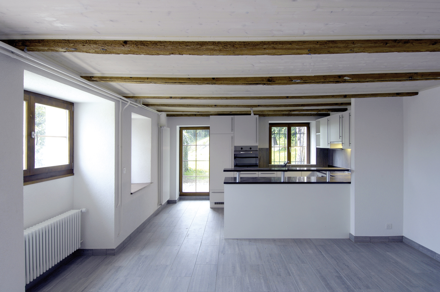 Pièce à vivre de la Ferme Creux avant emménagement, poutres apparentes et cuisine ouverte au fond