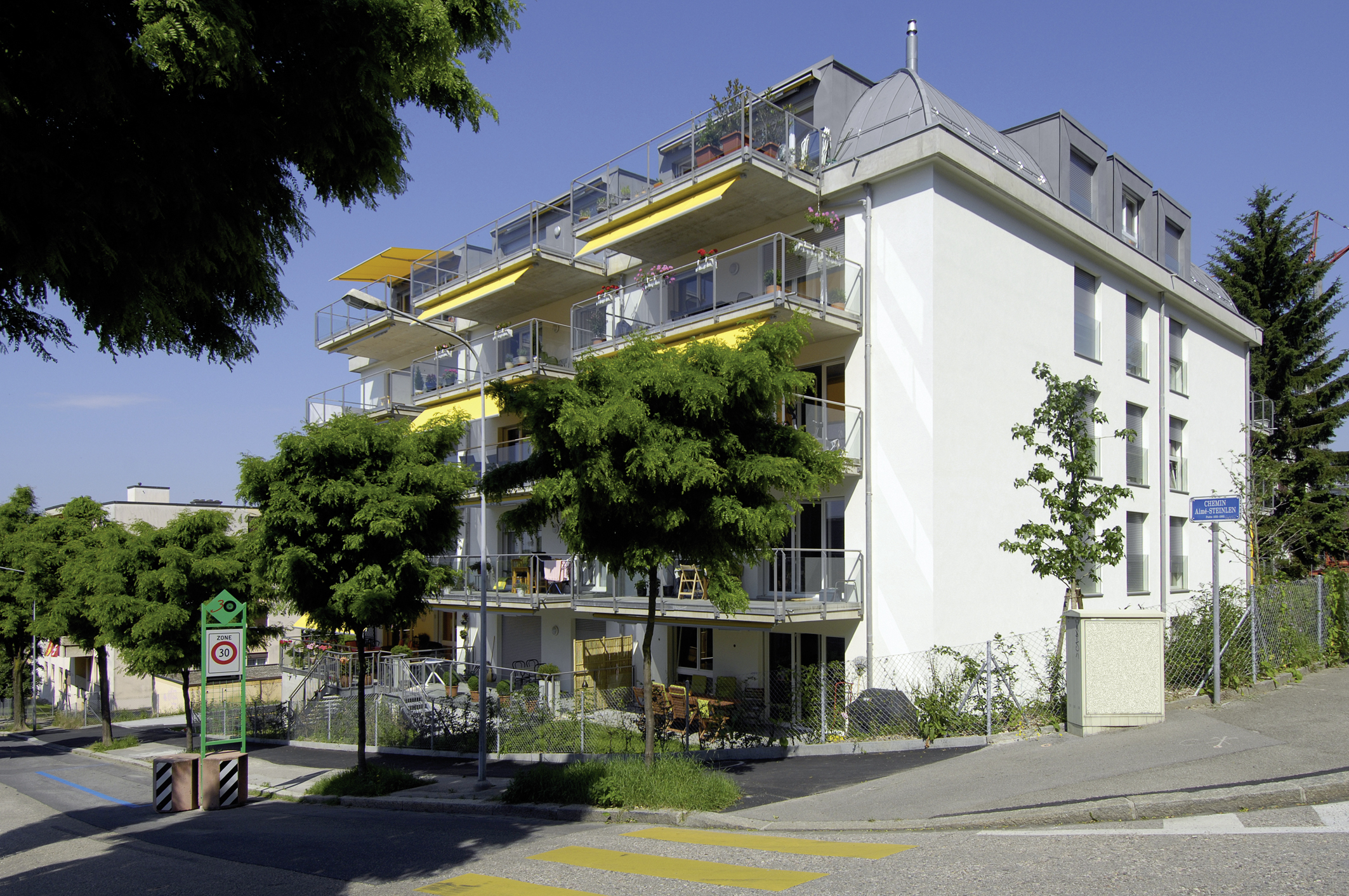 Immeuble des Balcons de Vallombreuse aux stores jaunes, vu depuis la rue bordée d'arbres