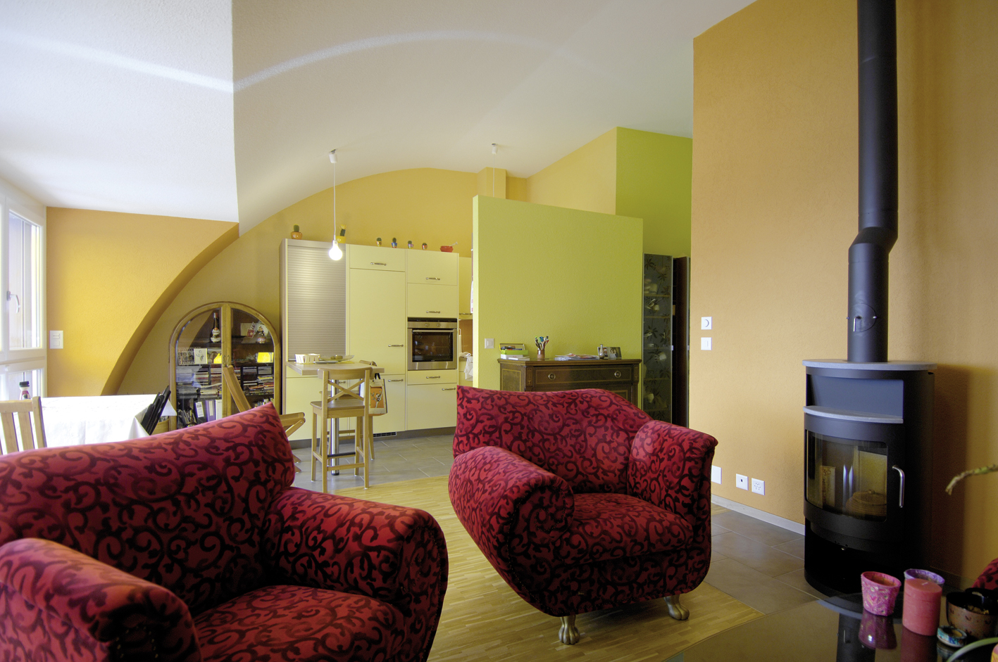 Séjour des Balcons de Vallombreuse, mur ocre voûté, cuisine vert anis et poêle à bois