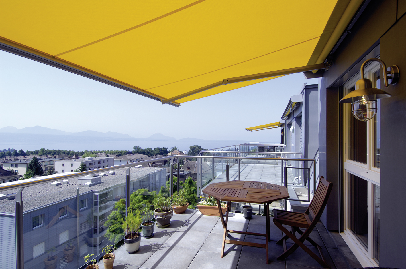 Terrasse des Balcons de Vallombreuse sous un store jaune, avec vue sur le lac