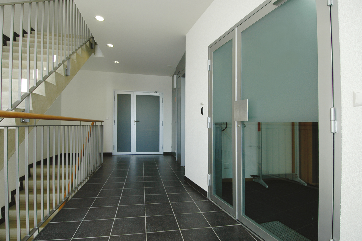 Palier carrelé de la résidence Sablons A avec porte vitrée et escalier
