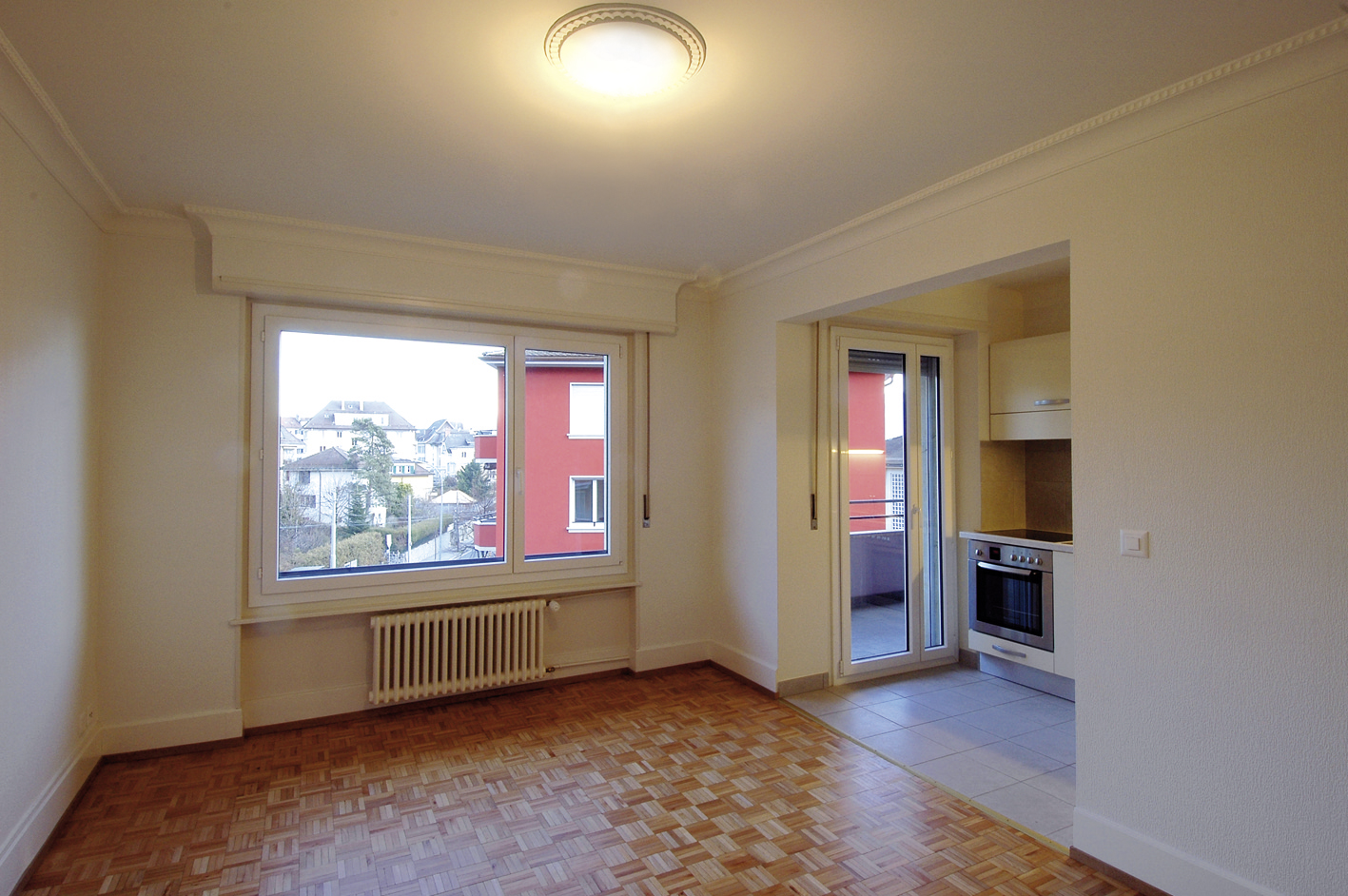 Séjour vide d'un appartement Marc-Dufour, parquet et fenêtre donnant sur la ville