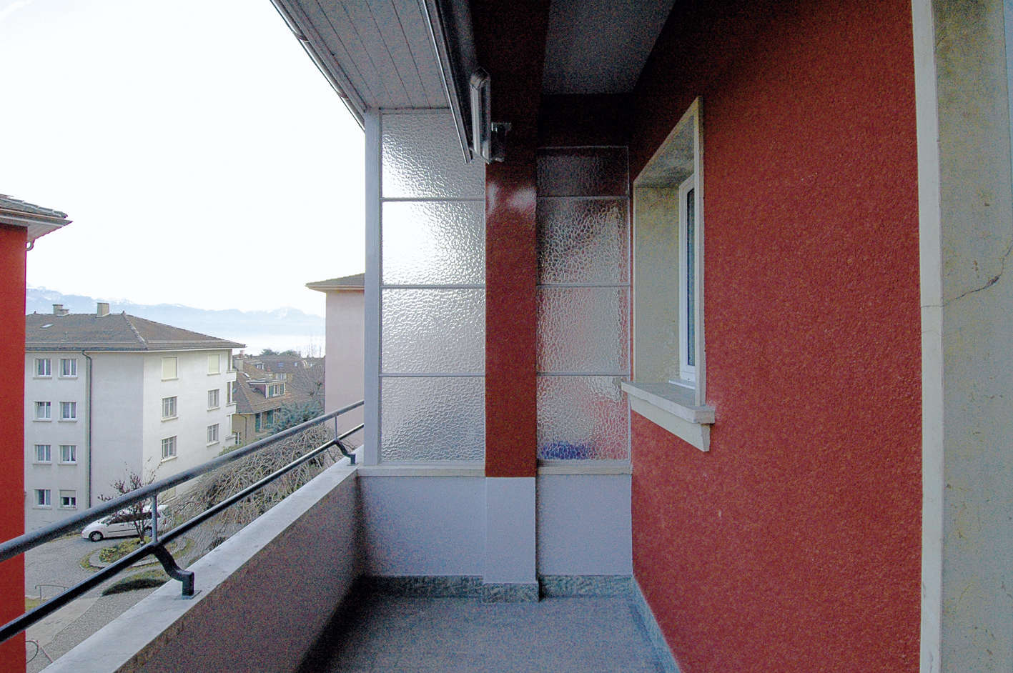 Balcon de l'immeuble Marc-Dufour et son crépi rouge, avec vue sur les toits