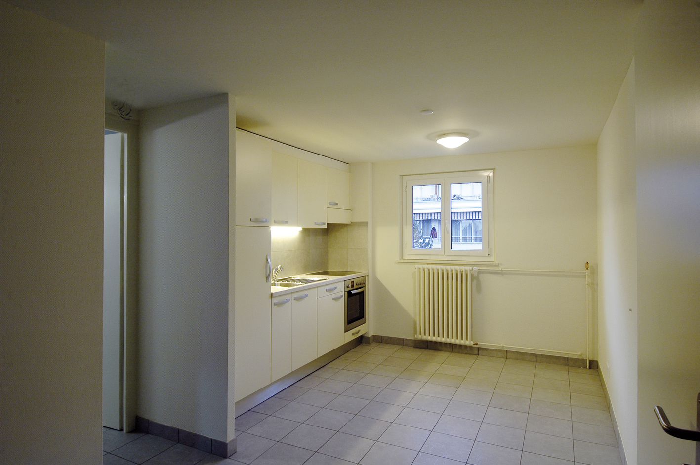 Cuisine blanche ouverte sur la pièce à vivre d'un appartement Marc-Dufour