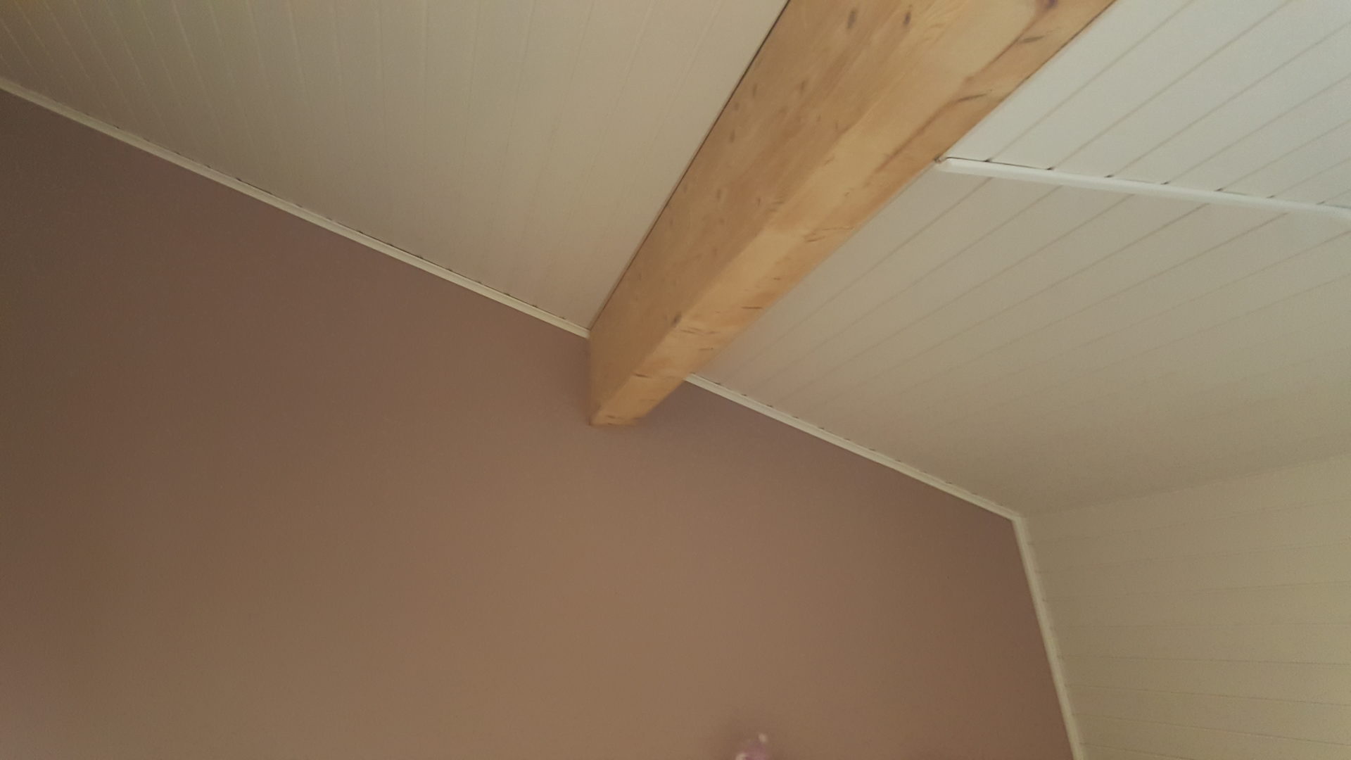 Chambre peinte en vieux rose sous un plafond lambrissé blanc et une poutre apparente