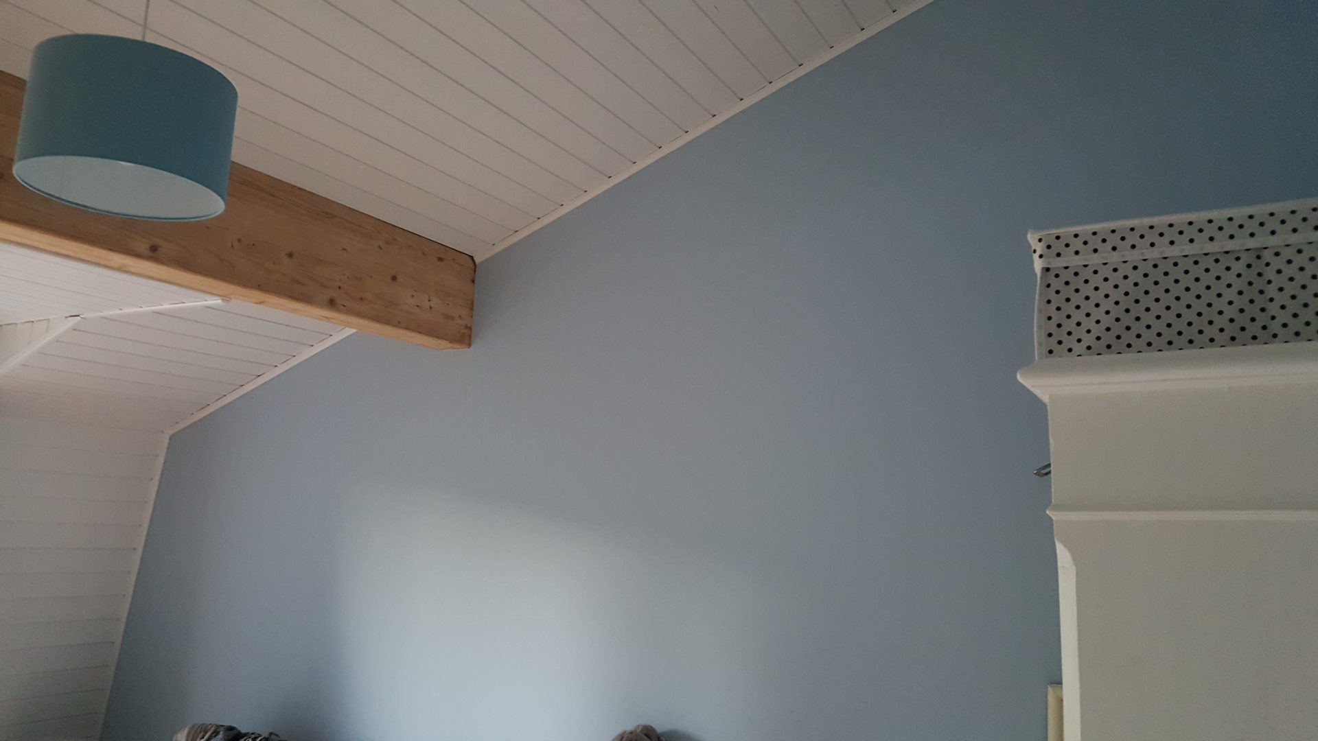 Chambre peinte en bleu-gris sous un plafond lambrissé blanc et une poutre apparente
