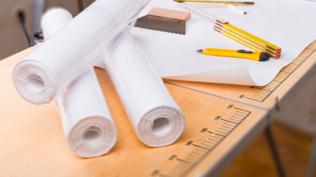 Rouleaux de papier peint, crayons, mètre pliant et cale à poncer posés sur un établi en bois