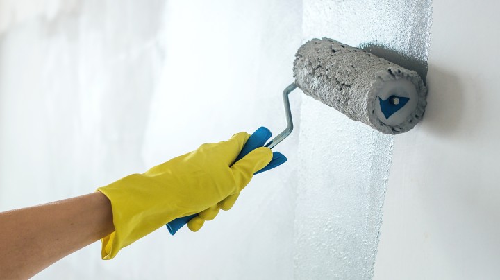 Main gantée appliquant au rouleau un enduit de rénovation épais sur un mur intérieur