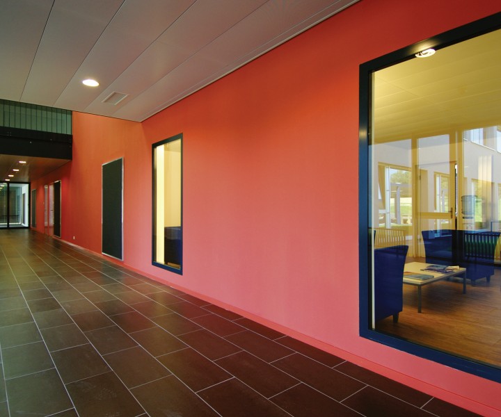 Couloir de l'International School of Lausanne, mur rouge et grande baie vitrée sur une salle de travail