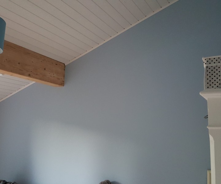 Chambre peinte en bleu-gris sous un plafond lambrissé blanc et une poutre apparente